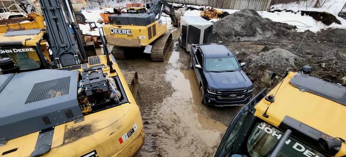Des pelles John Deere sur un chantier boueux, la camionnette et la remorque de Mécanique Vallières au milieu