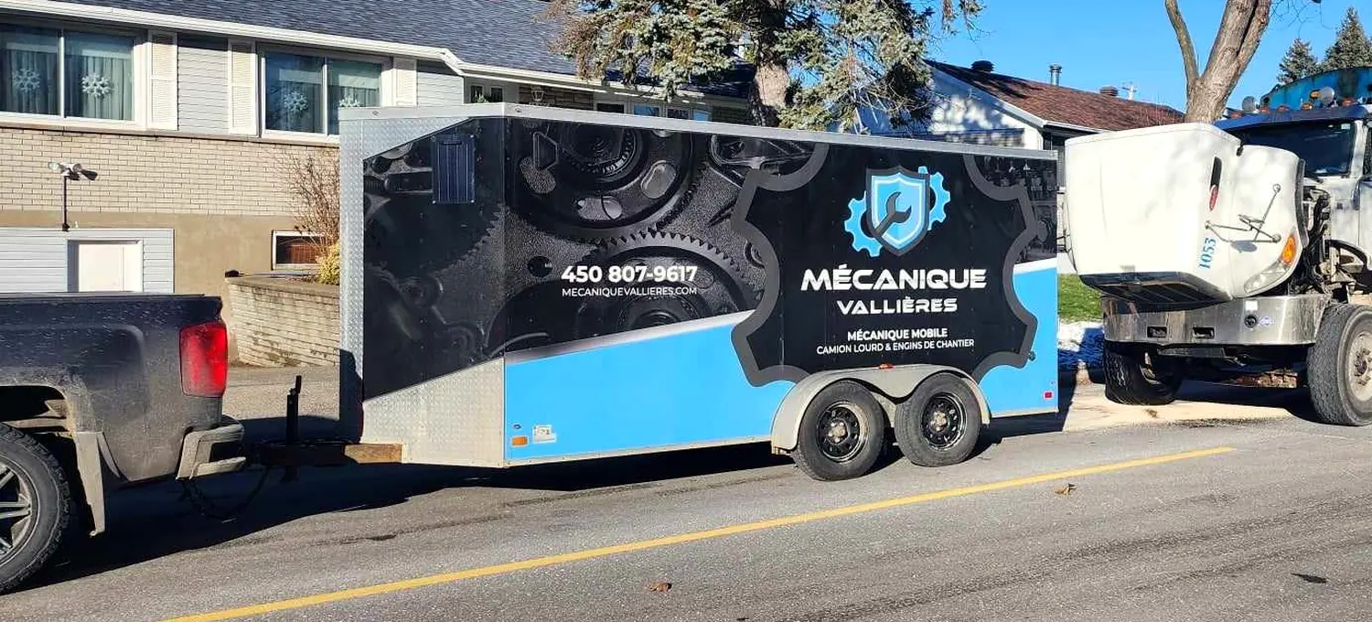La camionnette et la remorque lettrée Mécanique Vallières stationnées dans une rue, devant un camion au capot ouvert