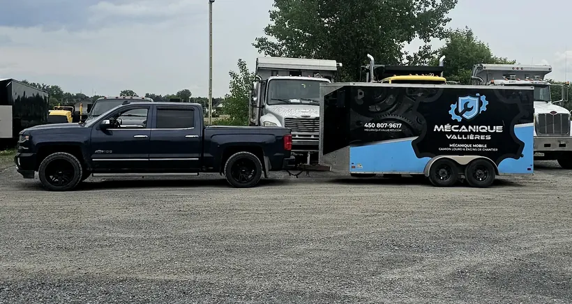 Le pick-up et la remorque-atelier de Mécanique Vallières dans une cour, devant des camions à benne