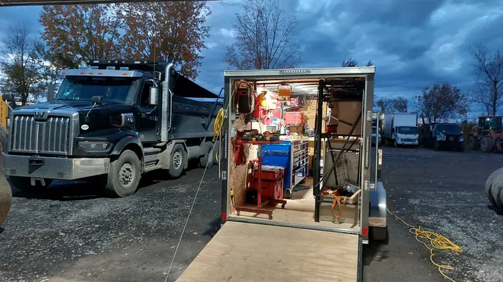 La remorque-atelier ouverte à côté d’un camion à benne, à la brunante