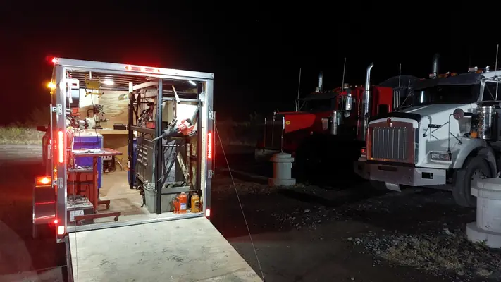 La remorque-atelier éclairée en pleine nuit devant deux camions lourds